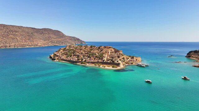 Kalydon Island, known as Spinalonga, shows Venetian fortifications and stone ruins surrounded by turquoise waters of Mirabello Bay near Elounda, Lasithi, Crete, Greece, drone pullback.