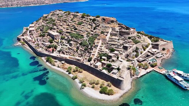 Spinalonga Island, ancient Kalydon, features Venetian fortifications, stone ruins and a harbor surrounded by turquoise waters in the Gulf of Mirabello, Lasithi, Crete, Greece, orbit establishing shot.