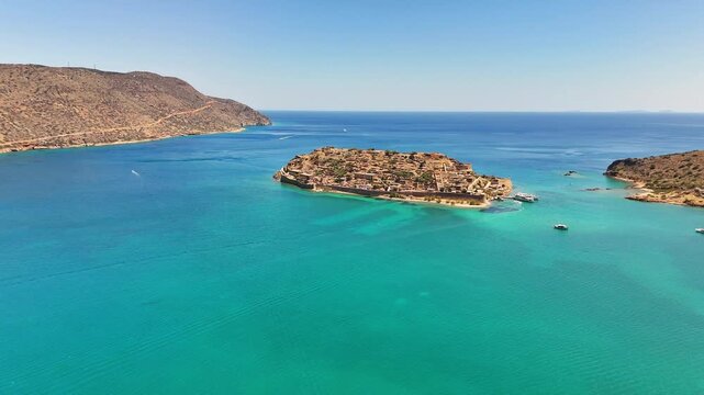 Spinalonga, officially Kalydon, rises as a fortified rocky island in the Gulf of Elounda, with Venetian walls and historic ruins surrounded by turquoise water, Crete, Greece.