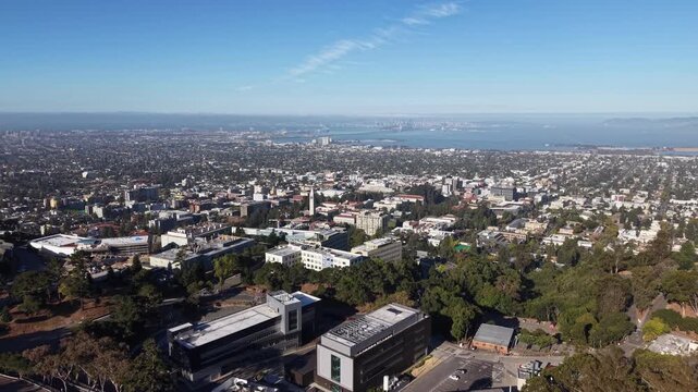 Panoramic aerial view flying over the University of California, Berkeley, campus with a clear sight of the San Francisco Bay, Oakland, and the city skyline on a sunny day in California