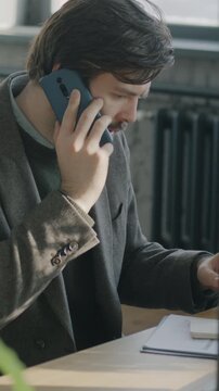 Young man office worker speaking on mobile phone and writing information in notebook in shared workplace. Business communication and cellphone call concept.