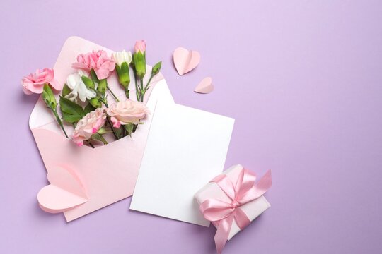 Beautiful carnations with gift box, paper envelope and white card on violet background with copyspace