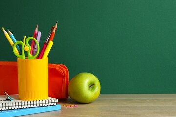 School-themed scene set against green background, with organized stationery, pencil holder, notebook, pencil case, scissors, and a green apple. Space for text © Sunlight