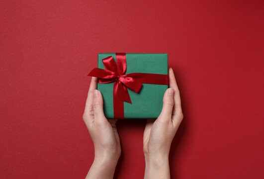 Close-up of a woman's hands holding a beautiful Christmas gift box against red background