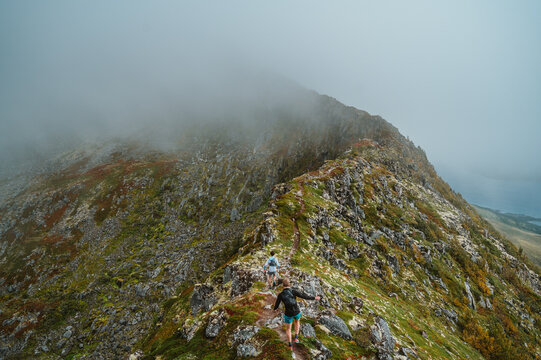 Two people trail run along a foggy mountain ridge