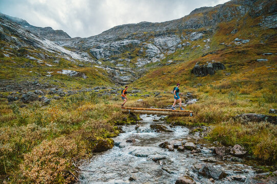 Two trail runners cross a log bridge in the mountains