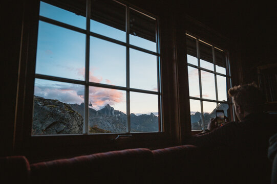 Man photographs mountain sunset from cozy cabin