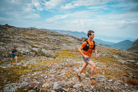 Two runners traverse a rocky mountain landscape