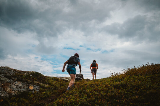 Two trail runners hiking up a rugged green hill