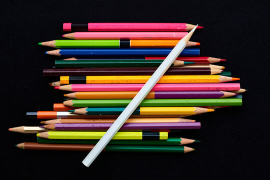 White colored pencil lying diagonally over pile of colorful pencils on black background