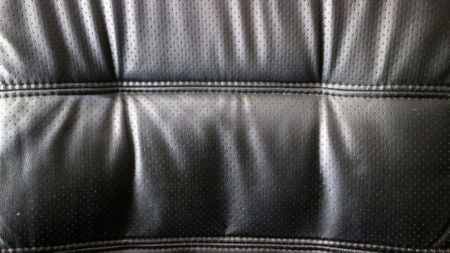 Close up texture of black perforated leather upholstery with stitched seams on an office chair seat
