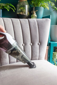 Hoovering vacuuming the upholstery on a grey chair with a handheld cordless vacuum cleaner. Household cleaning chores concept.