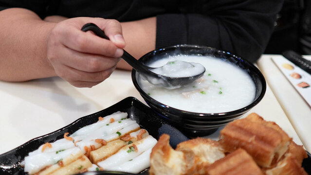 Person Eating Traditional Rice Congee with Rice Rolls and Dough Sticks