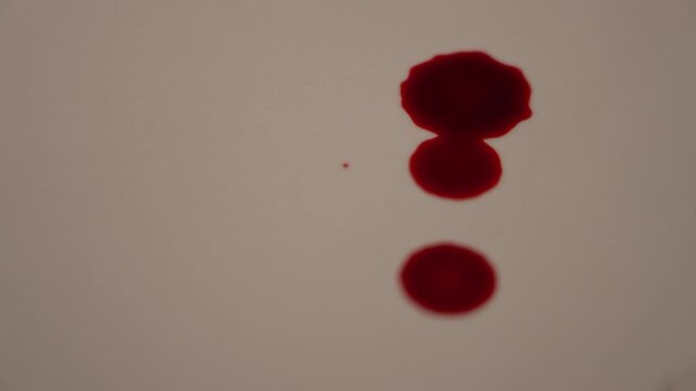 Extreme close up 45 degree view of continuous blood dripping on empty surface, spreading from right edge to center in slow motion, visceral horror 