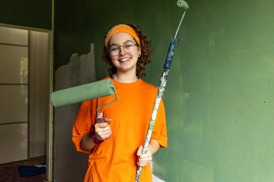 Smiling teenage girl holds paint rollers to paint her bedroom wall