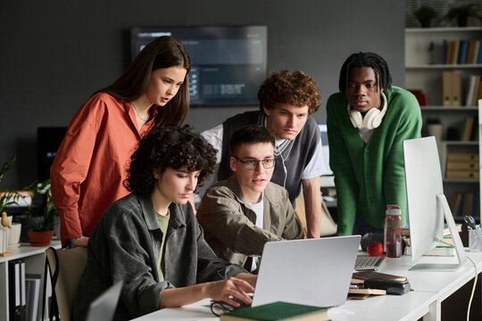Diverse students discuss a project on a laptop in a university class