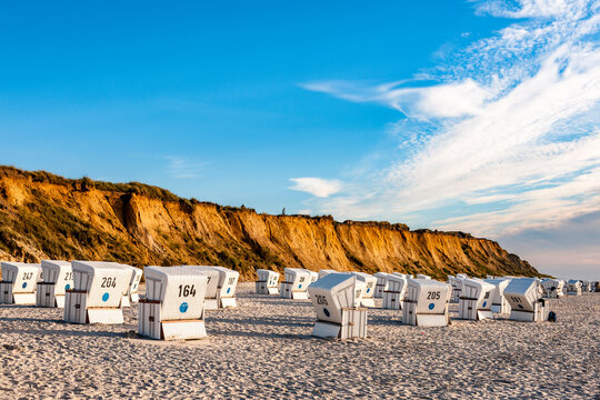 White beach chairs stand on the sand below the Red Cliff in Sylt