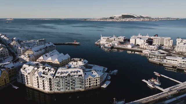 Cinematic aerial view of Alesund port in winter with snow covered buildings and calm sea water.