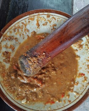 Traditional Indonesian peanut sauce sambal kacang being prepared in a stone mortar with wooden pestle. Used for gado-gado, pecel and satay. Concept of homemade cooking and Indonesian cuisine.