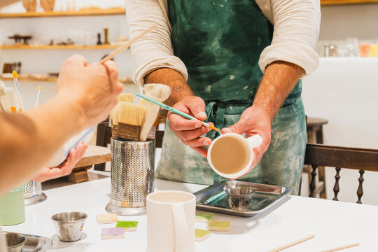 Male ceramist paints a handmade pottery mug during an art lesson