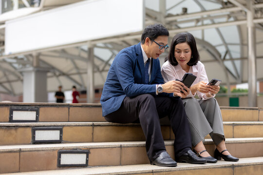 Two colleagues sitting outdoors, comparing smartphones and discussing digital information. business, smartphone, technology, colleagues, communication. Mobile business concept.