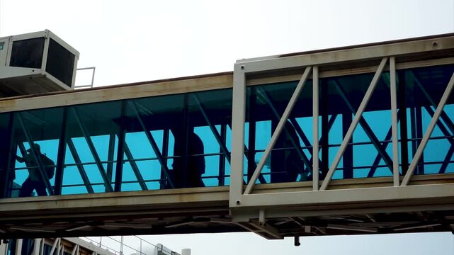 Modern airport glass aerobridge jetway corridor with silhouetted air passengers walking inside for airplane boarding concept of global air travel aviation industry and passenger transportation