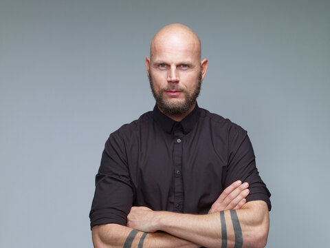 Portrait of man with bald and full beard in black in front of grey background