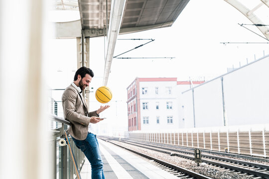 Smiling young man with cell phone and basketball at the station platform