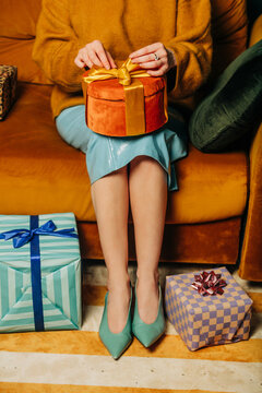 Stylish woman sitting on couch unwrapping a holiday gift