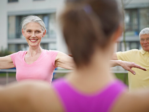 Senior woman and man exercise with an instructor outdoors