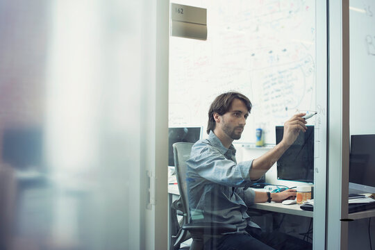 White collar worker sitting in office scribbling on glass wall