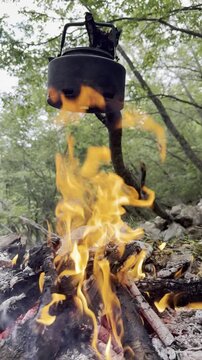 Vertical Orbiting Shot of a Teapot Hanging Over a Crackling Campfire