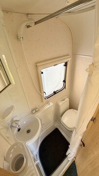 Compact caravan wet bath interior with toilet, sink and shower curtain inside a camper van