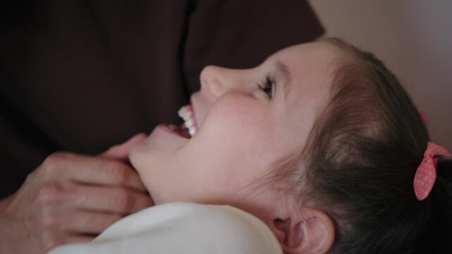 Close-up of a happy mother talking, laughing, and gently touching her young daughter lying down at home.