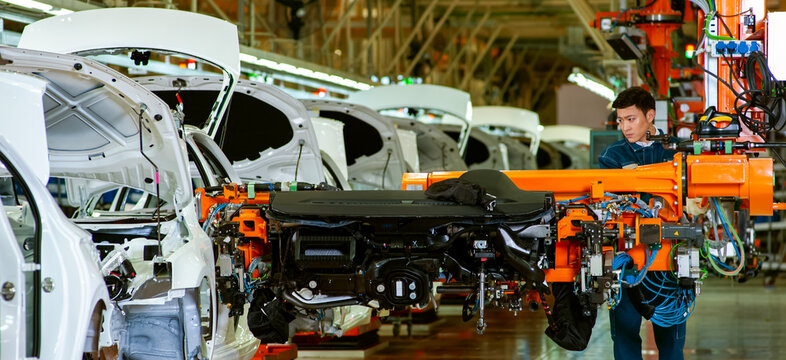 In a smart car factory's final assembly line, industrial workers operate automated robotic arms to assemble complete vehicles.