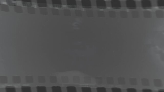 Vintage film strip rolling through projector showing blurred monochromatic historical archive footage.