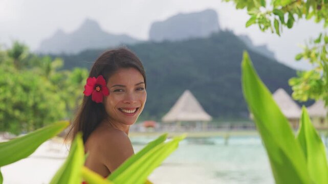 Beach beauty woman natural girl looking serene on tropical beach. Asian bikini model wearing hibicus flower body care wellness and spa pampering. Raw video of real woman model without makeup