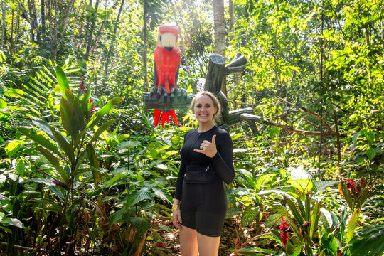 Woman standing in lush tropical garden with parrot statue