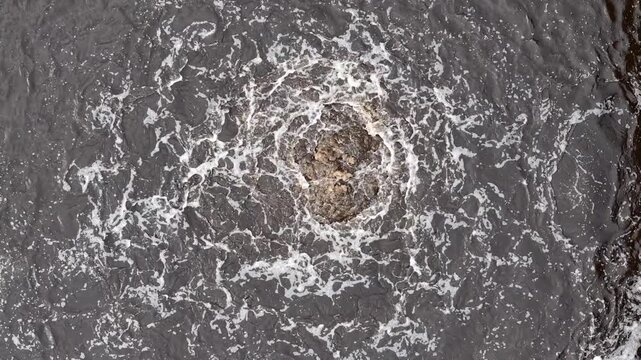 Top down aerial view of aerated wastewater basin with swirling foam and turbulent effluent at treatment plant
