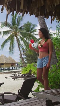 Tahiti hotel woman tourist drinking fruit drink cocktail at resort room balcony on beach. Vacation travel in Bora Bora, French Polynesia. Raw unedited vertical video of real woman model without makeup