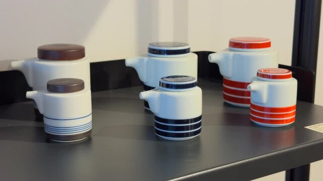 White ceramic soy sauce bottles with striped patterns and colorful lids arranged on a shelf, showcasing minimalist design.