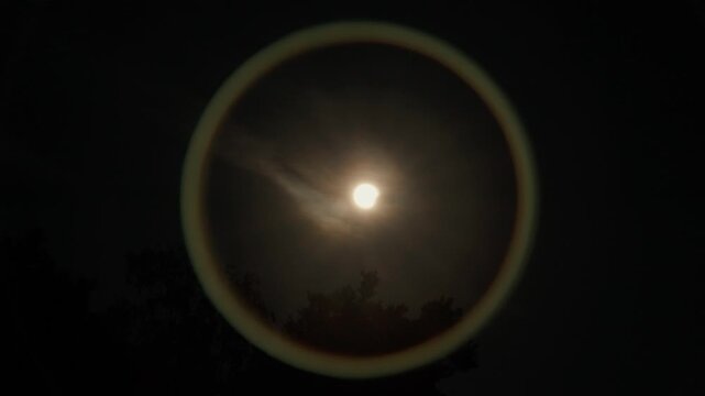 Start of the Solar Eclipse of 25.07.2026 the sun is slowly moving in front of the sun making a circular lens reflection on the lens just above some tree branches and clouds.
