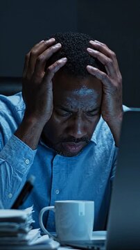 A Frustrated Man Struggles with Stress and Overwhelm While Working Late at His Desk, Battling an Unrelenting Workload and Anxiety in the Darkened Office Environment