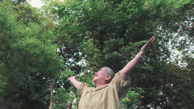 Happy senior asian woman breathing fresh clean air in urban park during summer wellness sunlight exposure, front view