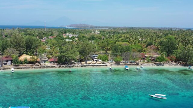 High aerial drone over clear blue-green water shows all of Gili Trawangan with its trees and buildings, Gili Air behind, Lombok, Indonesia. Cinematic Gili Islands establishing b-roll.