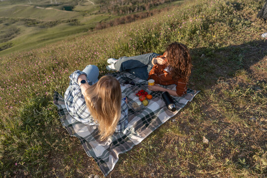 Picnic, women, meadow, two young friends relaxing on a blanket at a scenic mountain landscape during a sunny afternoon outing
