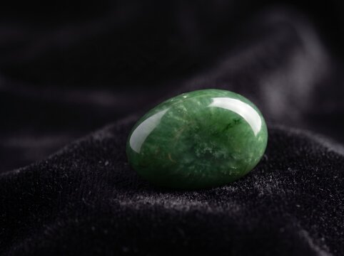 Polished green jade gemstone resting on black velvet fabric with elegant light reflection