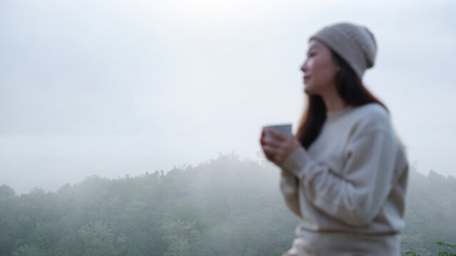 Blurred of a woman drinking drip coffee while sitting on wooden terrace with a mountain view on foggy morning