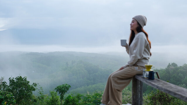 Blurred of a woman drinking drip coffee while sitting on wooden terrace with a mountain view on foggy morning
