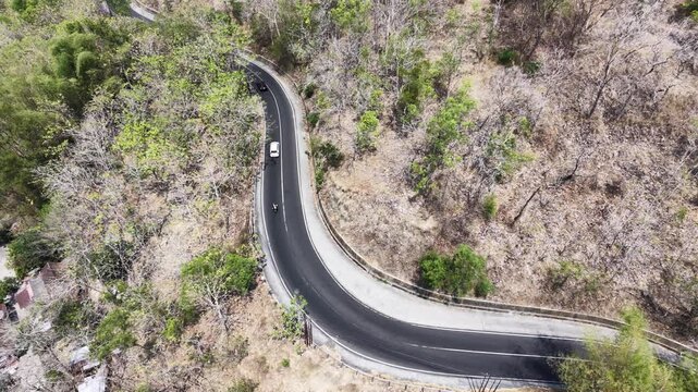 Slow motion bird's eye view from a drone looking straight down at a zig zag serpentine street in the hills. The empty paved pathway crosses through arid wilderness and sparse trees.